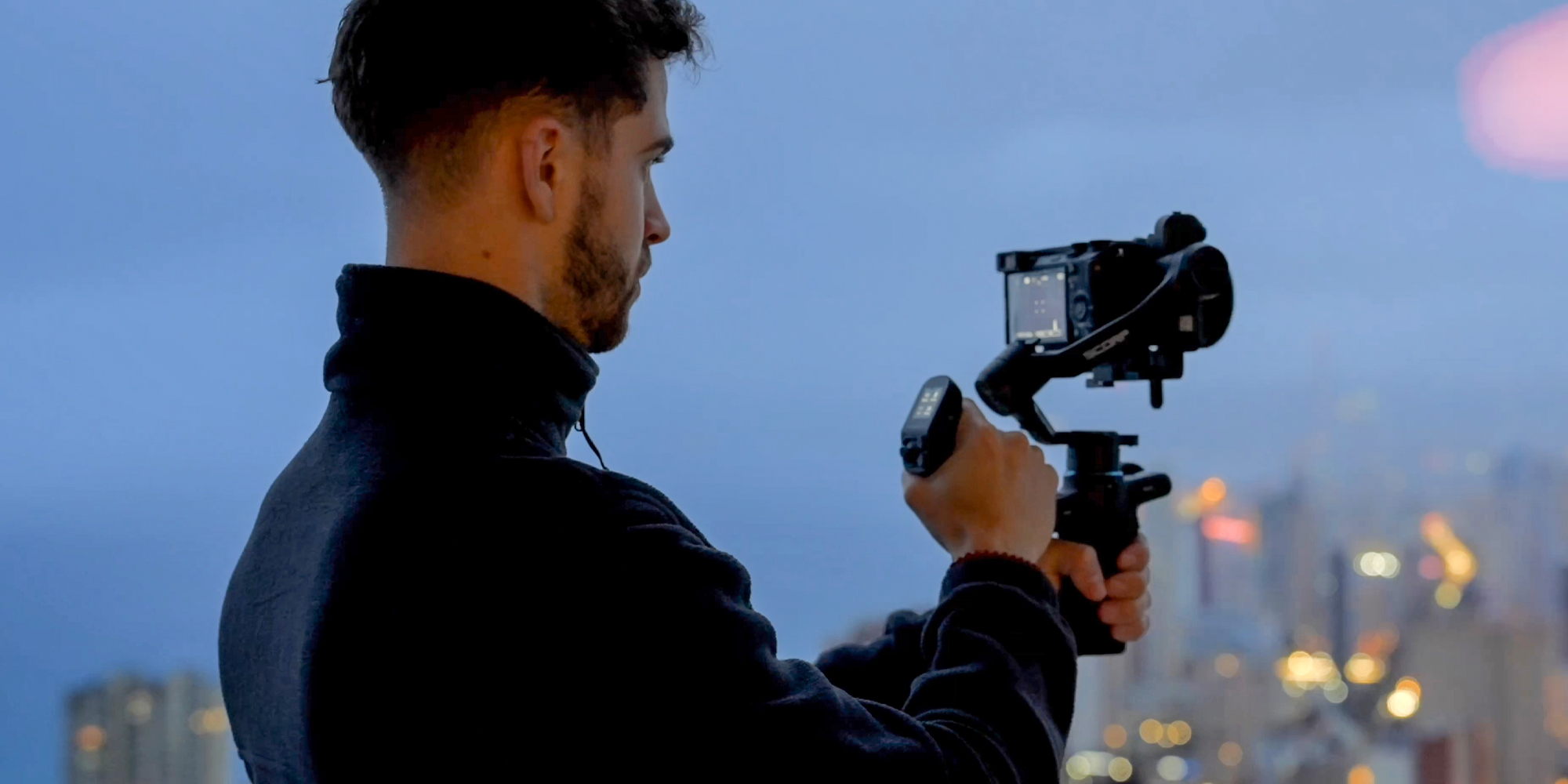 width=100% Gimbal ręczny FeiyuTech Scorp mini 3 Kit w rękach operatora filmującego w plenerze na tle nieba